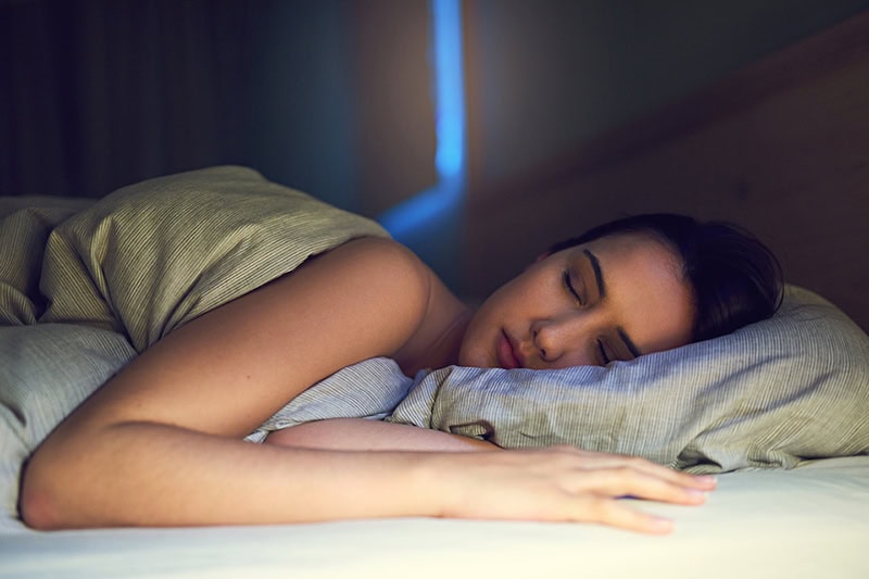 3 Health Benefits of Using Your AC While Sleeping. Photo of a woman sleeping in her bed.