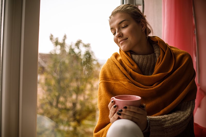 A women sitting in front of a window relaxing.